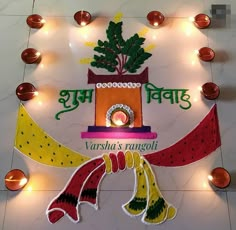 a decorated sign with lights around it and candles on the floor behind it that reads varsha's rangoli