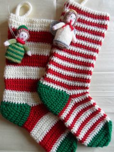 two crocheted christmas stockings hanging on a white wooden floor with one red and green striped stocking