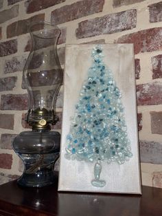 a glass christmas tree sitting on top of a wooden table next to a vase and lamp