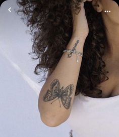 a woman with curly hair and butterfly tattoos on her arm is posing for the camera