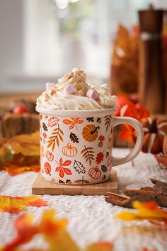 a cup filled with whipped cream sitting on top of a wooden table next to fall leaves