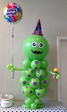 a green balloon in the shape of a caterpillar holding a candy bar and wearing a party hat