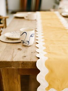 a wooden table topped with a white cup and saucer next to a yellow table cloth