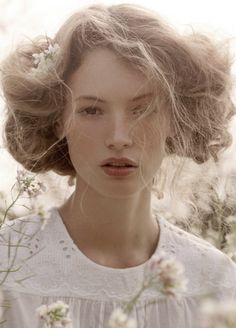 a woman with flowers in her hair is standing among the grass and wildflowers