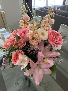 a vase filled with pink and white flowers on top of a glass table next to a couch