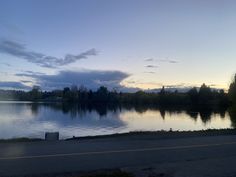 the sun is setting over a lake with trees in the background and clouds in the sky