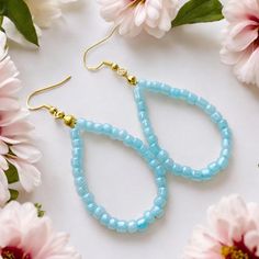 two blue beads are hanging from the ends of earrings on a white surface with pink flowers