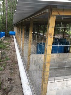 the inside of a fenced in area with blue barrels on each side and a metal roof