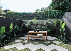 an outdoor living area with plants and a wooden table in the center, surrounded by grass