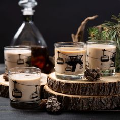 three candles sitting on top of a wooden table next to pine cones and an old fashioned decanter