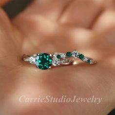 a woman's hand holding an emerald and diamond ring