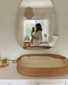 a woman taking a selfie in front of a mirror with a wicker bassinet