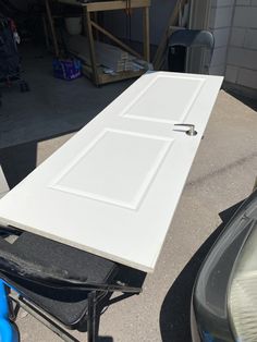 a white table sitting on top of a sidewalk next to a blue chair and a car