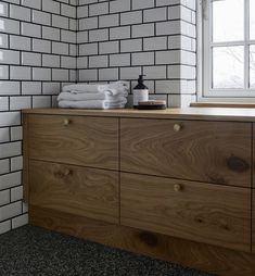 a bathroom with white brick walls and wooden drawers, along with towels on top of the dresser