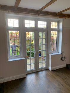 an empty room with double doors and wood flooring on the other side, looking out onto a back yard