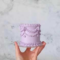 a hand holding a purple cake on top of a white plate