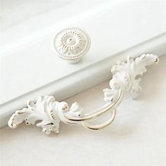 an ornate white door handle on the side of a window sill with a circular knob in the middle