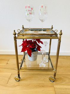 a gold serving cart with two wine glasses and a poinsetti in it on a wood floor