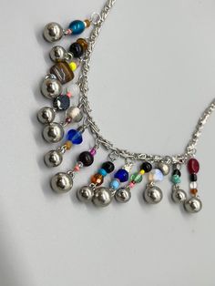 This unique necklace featuring colorful handmade beaded charms and silver balls will set the stage for any outfit you put on. Pair it with your favorite jeans or maxi skirt. Wear it year-round for unlimited styling options. It measures approx 20 inches in length and fastens with a lobster claw closure.  #uniquecolorfulnecklace #handmadebeadedcharmnecklace #doubleddezinez Multicolor Metal Beaded Necklaces, Multicolor Beaded Metal Necklaces, Multicolor Metal Beaded Necklaces For Party, Multicolor Metal Necklace With Beaded Chain, Multicolor Metal Necklaces With Round Beads, Multicolor Metal Necklaces With Unique Variations, Multicolor Metal Round Bead Necklaces, Multicolor Round Beads Metal Necklace, Multicolor Beaded Metal Necklace