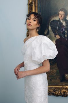 a woman standing in front of a painting wearing a white dress with puffy sleeves