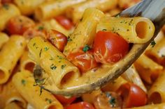 a spoon full of macaroni and cheese with tomatoes on the top is being held by a fork