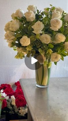 a vase filled with white roses on top of a table next to red and white flowers