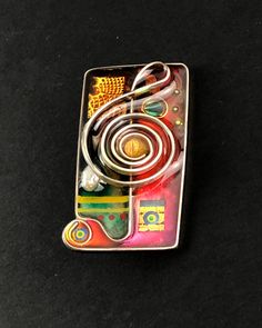 a small metal object on a black surface with some wires attached to it and an orange, yellow, green, red, and blue design in the center