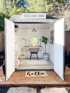 a small white shed with the door open to reveal a desk and chair in it