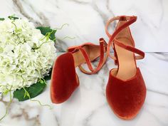 a pair of red shoes sitting on top of a white marble floor next to a bouquet of flowers