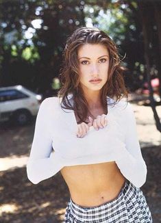 a young woman posing for a photo in front of a tree with her hands on her hips