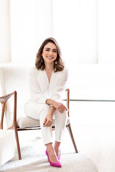 a woman sitting in a chair with her legs crossed and smiling at the camera while wearing pink shoes