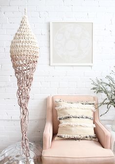 a pink chair sitting in front of a white brick wall next to a vase with flowers