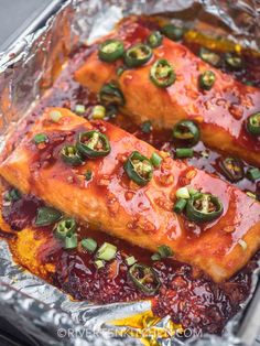 two pieces of fish covered in sauce and green peppers on top of tin foil with seasoning