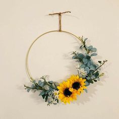 a sunflower and eucalyptus wreath hanging on a white wall with a twig in the middle