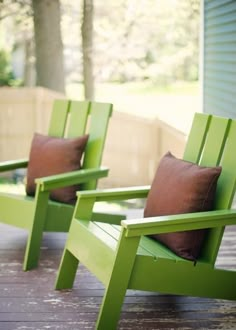 two green chairs sitting on top of a wooden deck next to each other with brown pillows