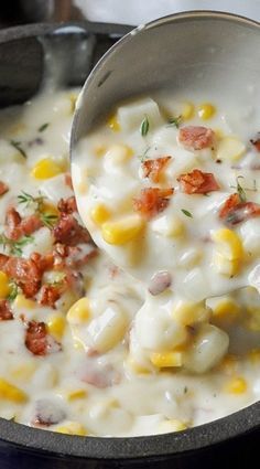 a pot filled with corn and cheese on top of a stove next to a spoon