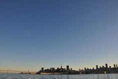 an airplane is flying over the water in front of a cityscape and bridge