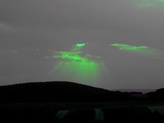 the sky is lit up with green light as it sits on top of a hill