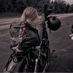 two people riding motorcycles on a road with trees in the background and one person wearing a leather jacket