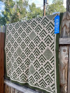 a green and white afghan hanging on a fence next to a wooden fence with a blue sign