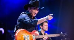 a man wearing a cowboy hat and holding a guitar on stage with another man in the background