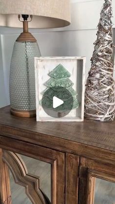 a christmas tree sitting on top of a wooden table next to a glass vase and lamp