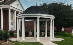 a white gazebo sitting on top of a lush green field next to a building