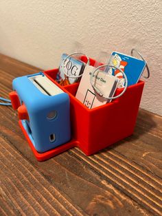 a red and blue container filled with books on top of a wooden table