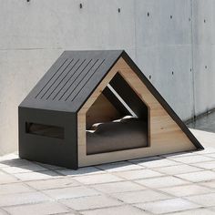 a dog house with a bed in it on the ground next to a concrete wall