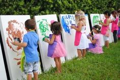 several children are painting on the side of refrigerators in front of some bushes and trees