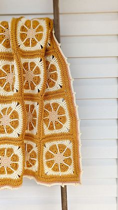 an orange crocheted blanket hanging on a clothes rack in front of a white wall