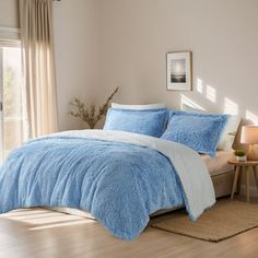 a bed with blue comforters and pillows in a room next to a window,