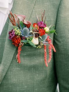 a man wearing a green suit with red and purple flowers on his lapel flower