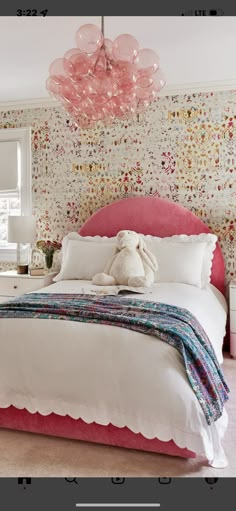 a bedroom with a pink bed and floral wallpaper on the walls, along with a teddy bear sitting at the foot of the bed